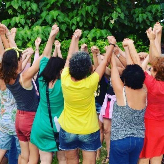 A circle of women holding hands outdoors.
